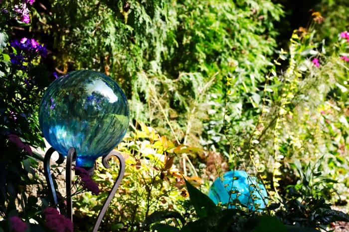 Une boule de verre bleue est assise sur un socle dans un jardin vert luxuriant, près d'une autre sphère bleue.