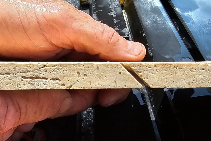 Une personne montre le bord d'un carreau qui a été coupé à un angle de 45 degrés à l'aide de la scie à carreaux humide DeWalt de 10 pouces.