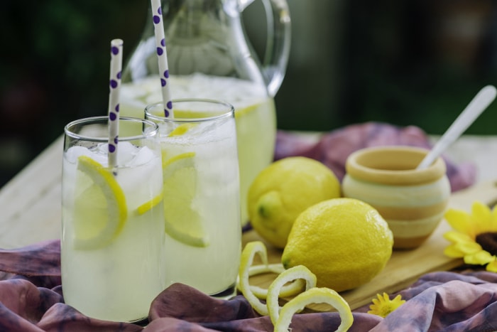 Un pichet de limonade fraîche faite maison accompagné de citrons et de verres pleins de limonade.