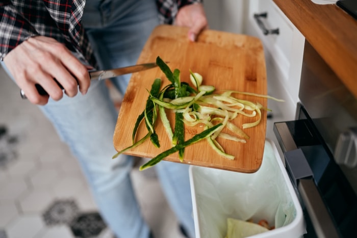 Une femme gratte les restes de légumes dans un bac de recyclage et de compostage des matières organiques dans une cuisine.