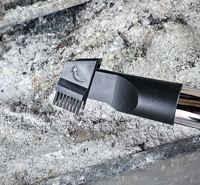 La brosse de l'aspirateur de cendres PowerSmith devant un tas de cendres dans un foyer.