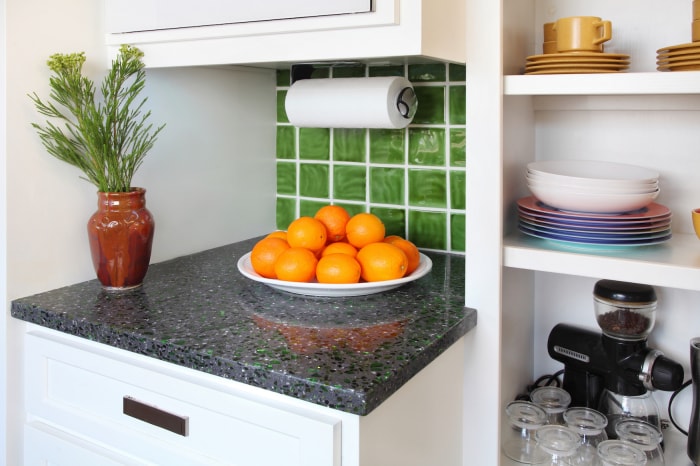 Un petit comptoir de cuisine avec un bol d'oranges à côté d'une étagère ouverte avec des tasses, des assiettes et des appareils électroménagers.