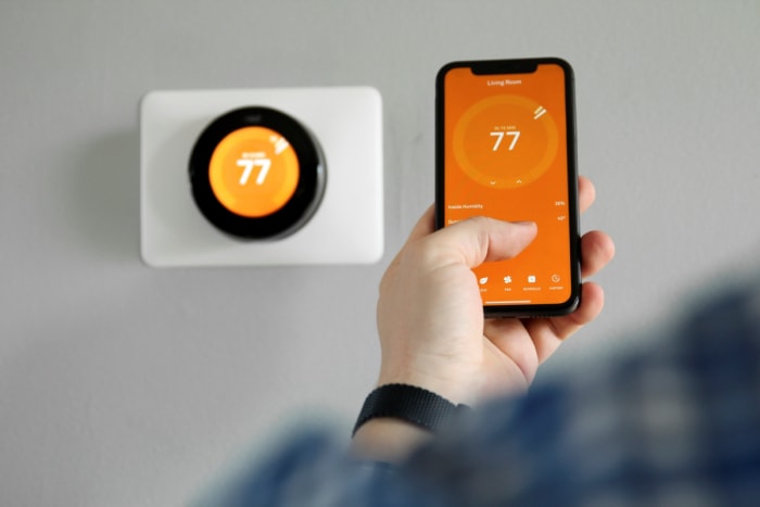 Personne utilisant un thermostat intelligent via son téléphone.