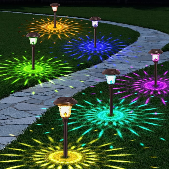 chemin de pierre sinueux éclairé par des lumières multicolores projetant des motifs sur l'herbe