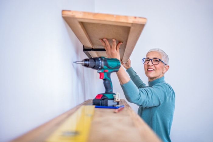 Une personne tient une étagère en bois pendant qu'elle l'installe en utilisant une perceuse.