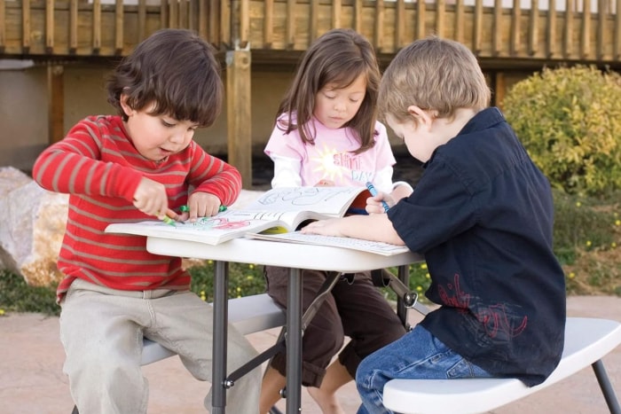 Trois enfants colorient des livres assis à la table de pique-nique pour enfants Lifetime.