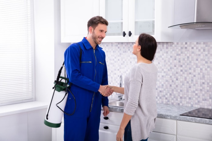 Un homme en costume de travail bleu portant un outil de lutte antiparasitaire serre la main d'une femme.