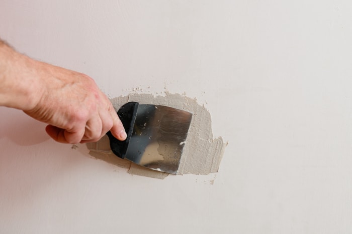 Une personne recouvre un petit trou dans un mur avec de l'enduit