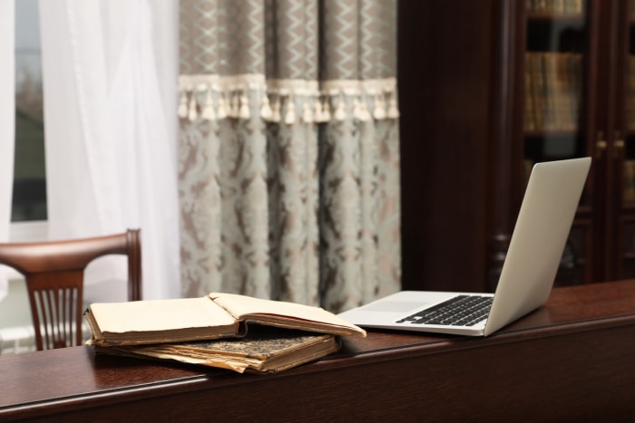 Un ordinateur portable ouvert est posé sur un rebord en bois, à côté de livres anciens et de meubles anciens.