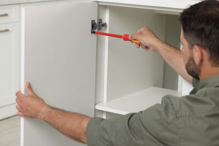 Un homme utilise un tournevis pour installer de nouvelles charnières de porte d’armoire de cuisine.