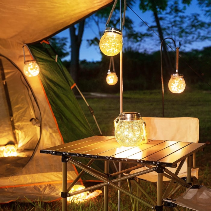 vue rapprochée du camping avec tente et table couverte éclairée par des lanternes à guirlandes chaudes