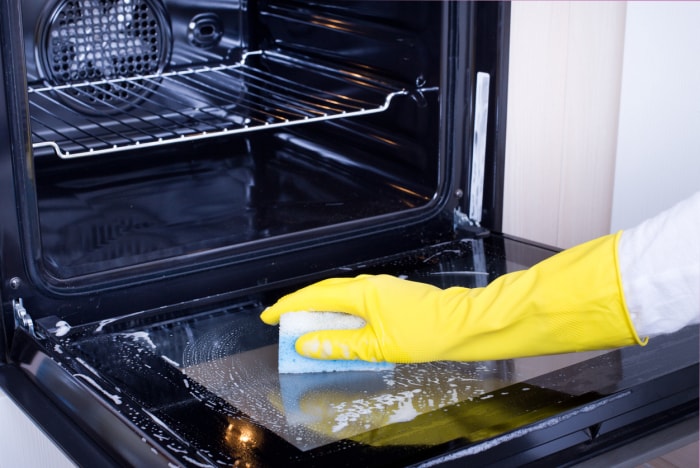 Gros plan d'une main de femme portant des gants de protection jaunes nettoyant la porte du four