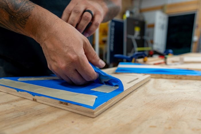 Personne utilisant du ruban adhésif bleu pour protéger le cadre en bois.