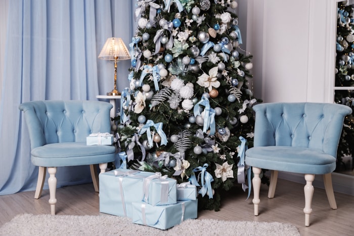 L'arbre de Noël sur le thème bleu et blanc, avec des rubans et des branches fleuries, est assis entre deux chaises bleues en velours.