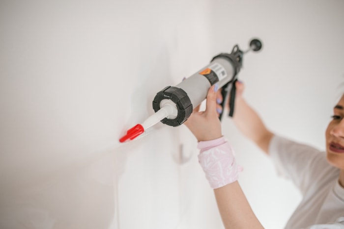 Une femme millénaire joyeuse vêtue d'un t-shirt blanc se tient debout dans un appartement vide, prête à peindre les murs