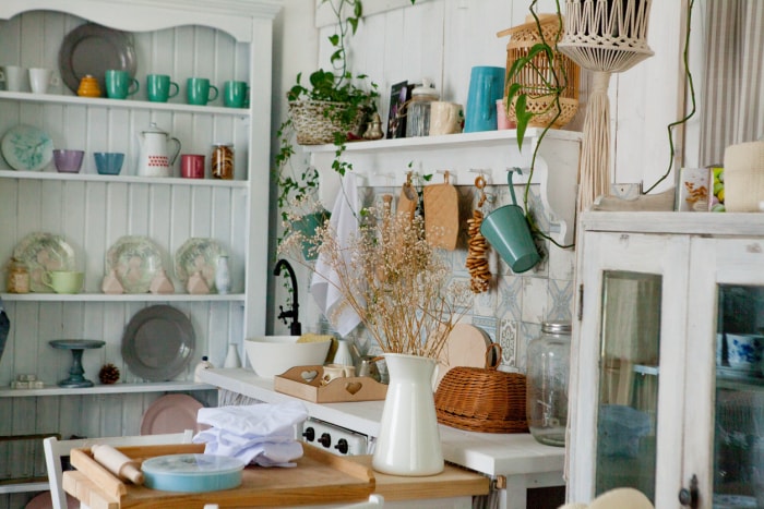 A-collection-of-vintage-dishes-and-mugs-is-displayed-on-shelves-in-a-cluttered-cozy-kitchenette.