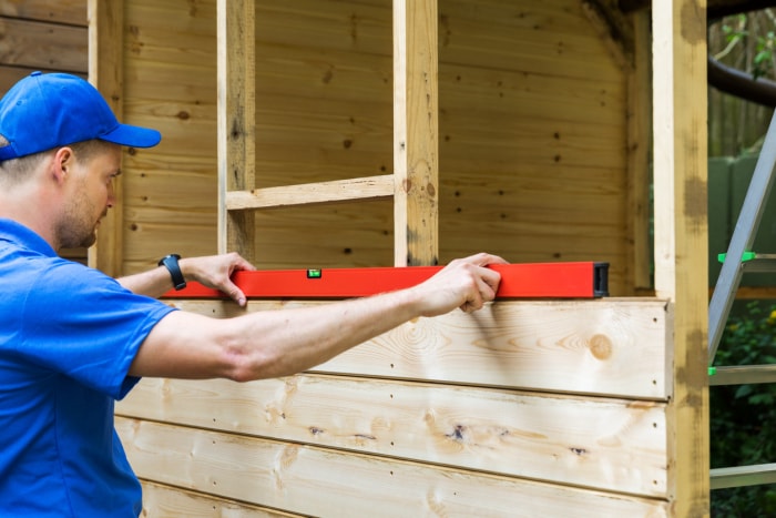 un homme utilise un niveau pour construire un hangar en bois