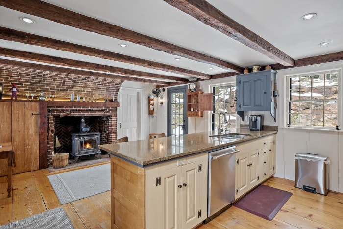 Une salle de séjour moderne à l'intérieur d'une maison résidentielle juste à côté de la cuisine avec un poêle à bois à l'intérieur d'une cheminée historique.