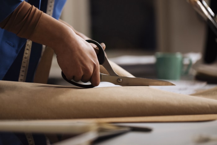 mains de femme coupant du papier brun avec des ciseaux