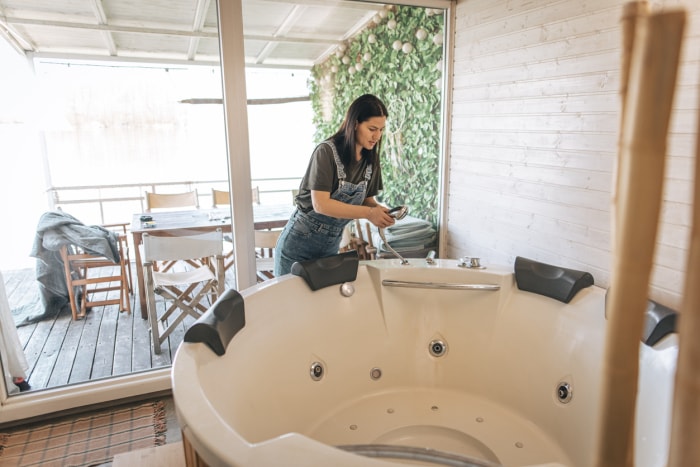 Une femme tenant la buse de douche d'un jacuzzi intérieur vide.