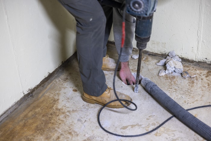 Installation d'un système d'atténuation du radon. Un ouvrier fait un trou dans le plancher du sous-sol pour améliorer la maison.