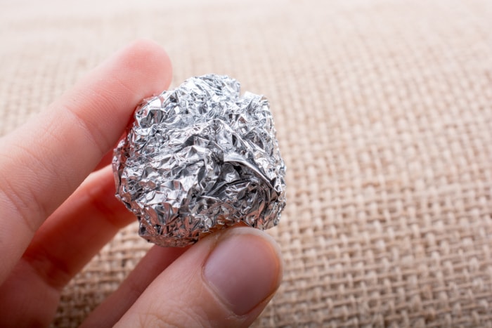 Une main tient une petite boule de papier d'aluminium sur un fond en tissu.