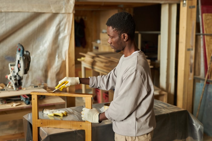 Portrait de côté d'un jeune homme afro-américain rénovant des meubles en bois dans un atelier