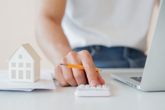 Une personne calcule les mensualités hypothécaires à l’aide d’une calculatrice et d’un ordinateur portable.