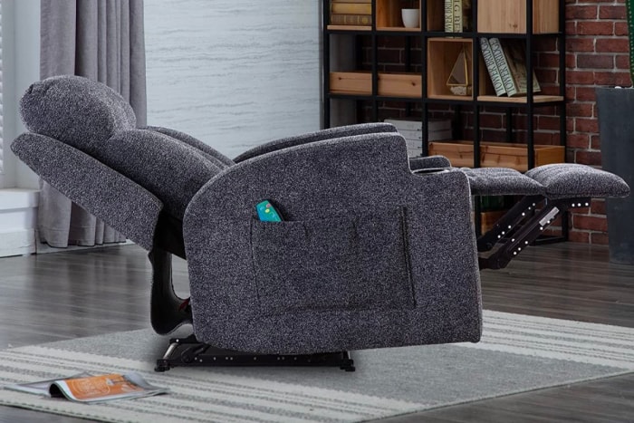 Un fauteuil inclinable gris en position inclinée avec sa télécommande dans une poche latérale