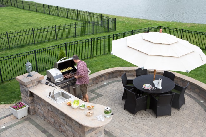 Homme d'âge mûr cuisinant sur un gril dans une cuisine extérieure en plein air avec un ensemble complet de patio couvert.