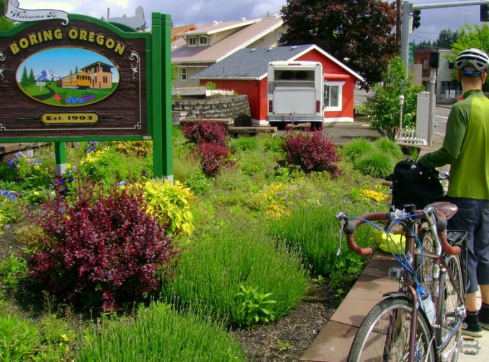 homme à vélo près d'un panneau indiquant un ennui en Oregon, avec une ferme en arrière-plan