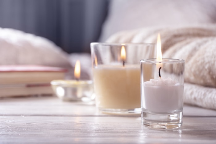 gros plan sur trois bougies de couleur claire avec des flammes sur un plancher en bois clair devant un lit flou et des livres