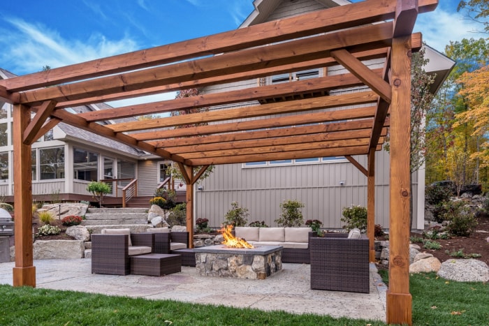 Une pergola en bois se dresse au-dessus d'un foyer carré et d'un ensemble de meubles d'extérieur assortis.