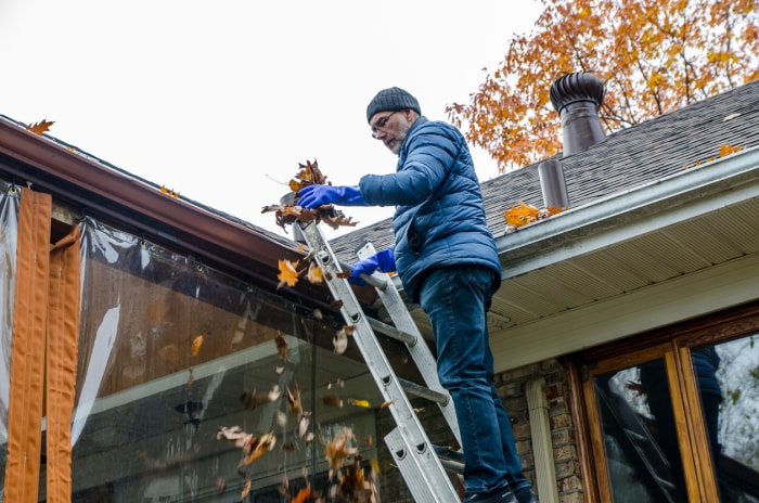 homme sur une échelle nettoyant les feuilles de la gouttière du toit