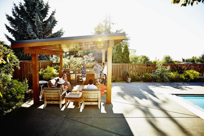 A group of friends eating under a wooden cabana in a backyard.