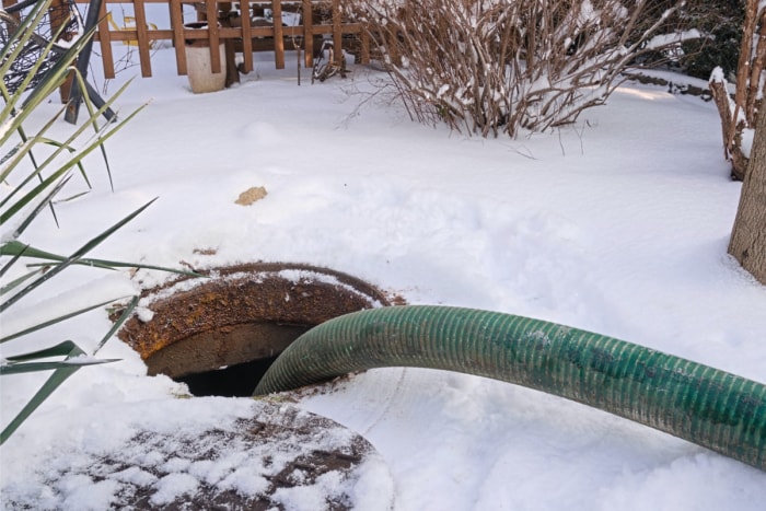 Tuyau septique épais descendu dans une fosse septique, entouré de neige au sol.