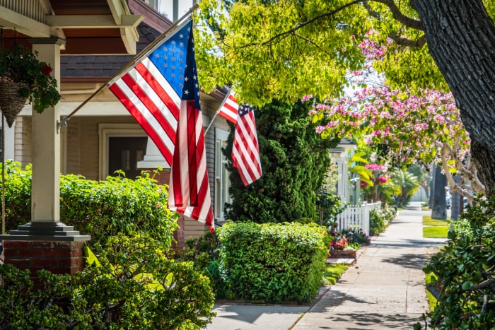 rue résidentielle avec des arbres et deux drapeaux américains suspendus aux maisons voisines