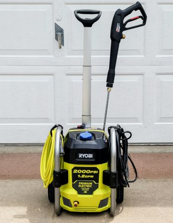 Le nettoyeur haute pression Ryobi 2000 PSI devant une porte de garage avec tous les outils et cordons embarqués soigneusement rangés