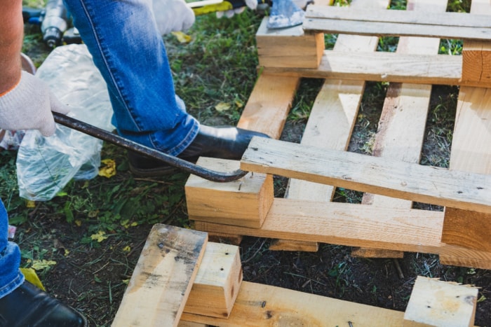 Une personne casse une palette en bois en utilisant un pied de biche et son pied.