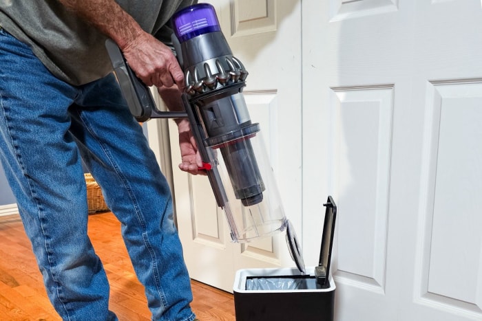 Une personne vide le bac à poussière de l'aspirateur sans fil Dyson Outsize dans une petite poubelle.