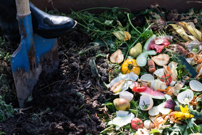 Un ouvrier creuse un bac à compost à l'extérieur rempli de déchets bruns et verts du jardin et de déchets alimentaires.