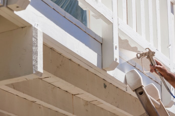 Gros plan d'un professionnel utilisant un pulvérisateur de peinture pour appliquer de la peinture blanche sur une terrasse en bois.