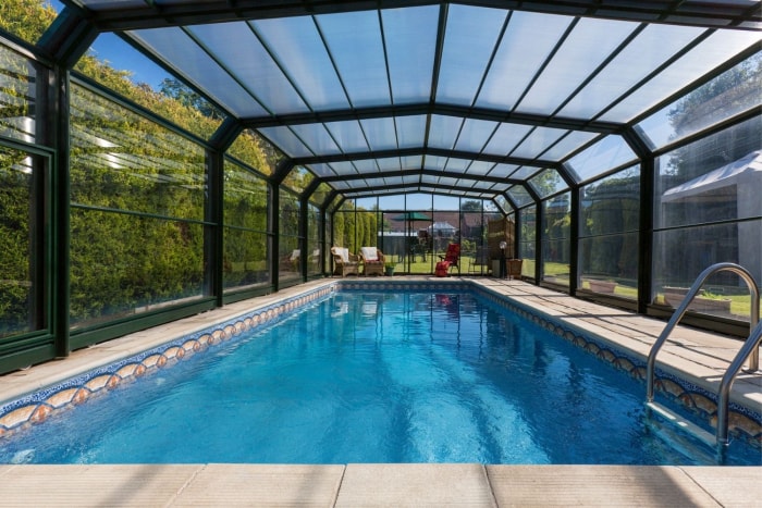 Une piscine creusée dans l'arrière-cour avec un abri de piscine en verre et noir.