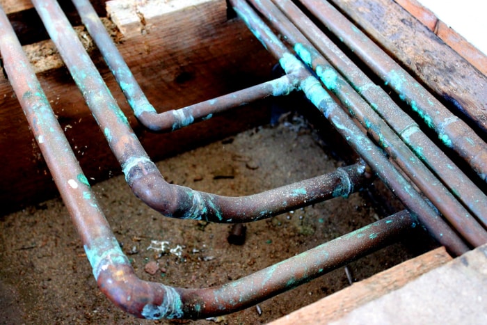 Photo en gros plan de vieux tuyaux en cuivre de radiateur de chauffage central sous le sol et de tuyaux d'eau chaude - départ, retour, chaud et froid.