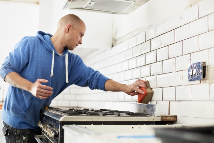 Un homme portant un sweat à capuche bleu applique du coulis sur le dosseret de la cuisine.