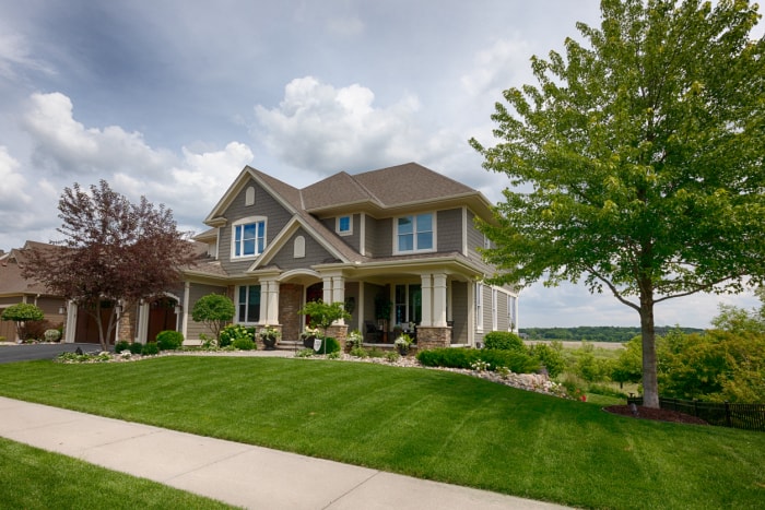 large suburban house with manicured lawn with a small tree at the end of the yard