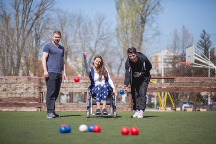 Une jeune femme en fauteuil roulant et ses amis jouent à la pétanque.