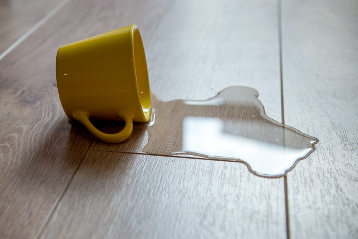 Une tasse jaune est renversée et de l'eau se répand sur un sol en bois stratifié.