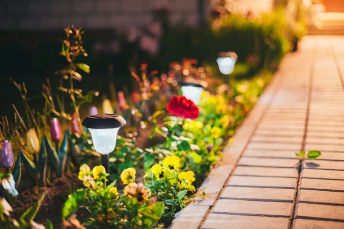 Une allée en briques bordée de lumières extérieures et de fleurs lumineuses.