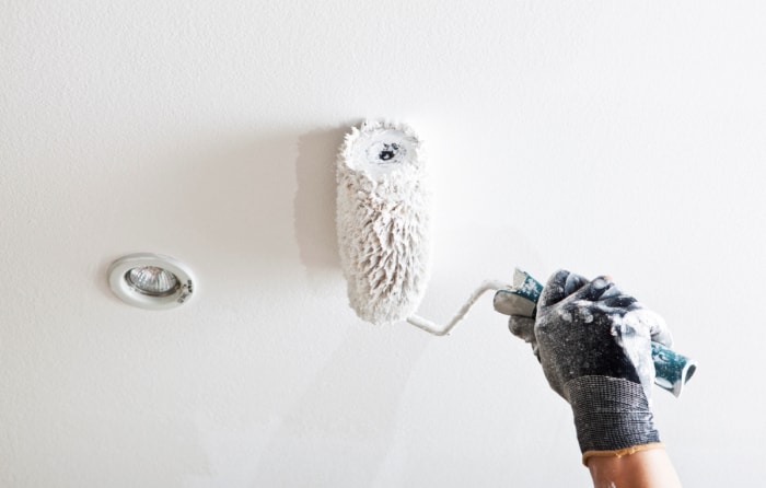 Main gantée utilisant un rouleau pour peindre le plafond.